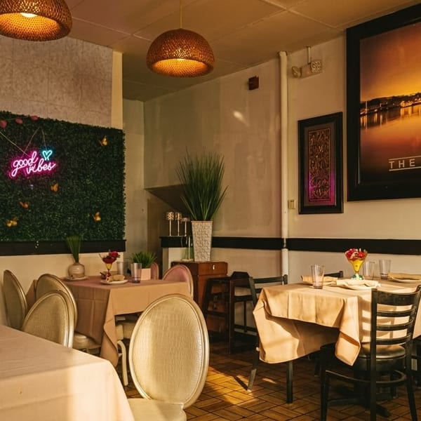 Restaurant interior with set tables, a neon "good vibes" sign on a green wall, and large artwork.
