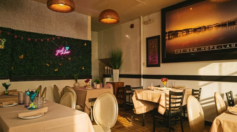 Restaurant interior with set tables, a neon "good vibes" sign on a green wall, and large artwork.
