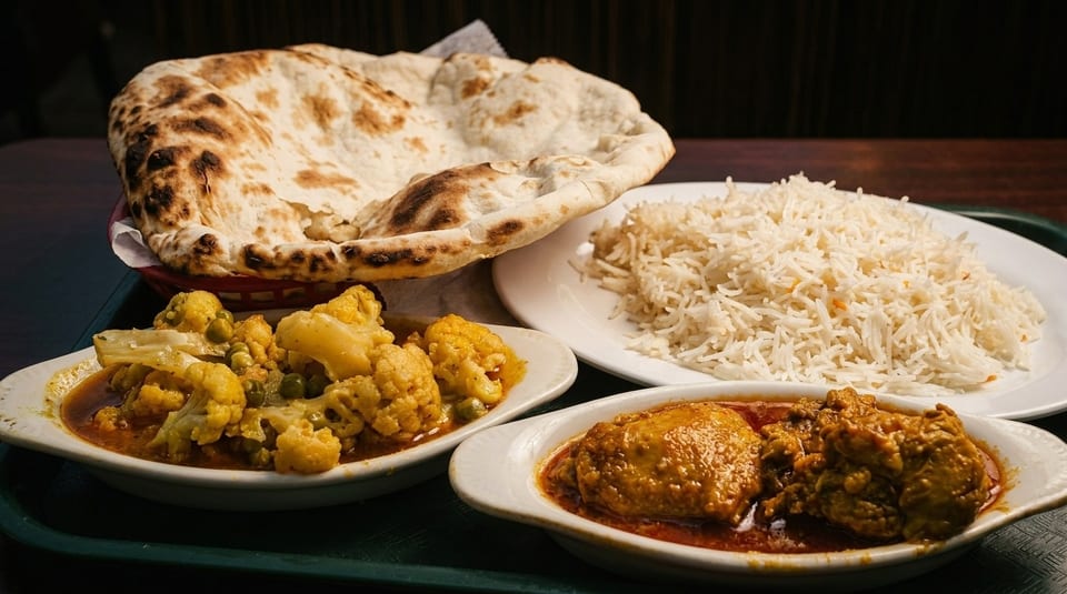 Indian meal with naan bread, white rice, cauliflower curry, and chicken curry on a tray.