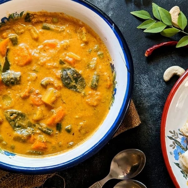 A bowl of vibrant vegetable curry with flatbreads, cashews, and curry leaves on a dark surface.