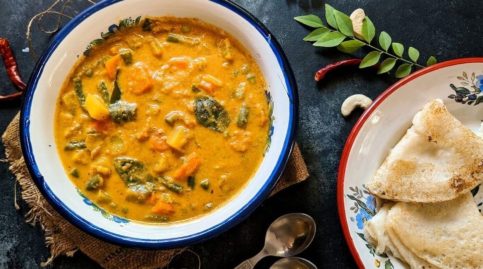 A bowl of vibrant vegetable curry with flatbreads, cashews, and curry leaves on a dark surface.