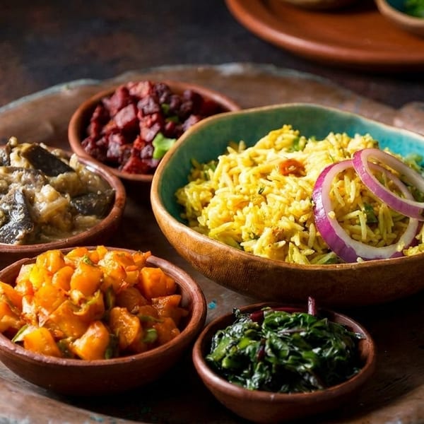 A copper tray holds five small bowls of colorful Indian food, including yellow rice with red onions.