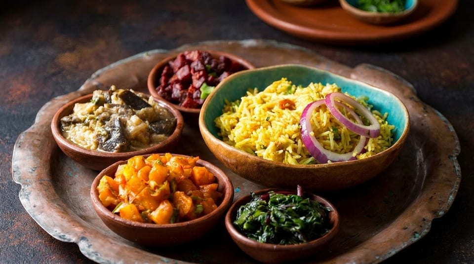 A copper tray holds five small bowls of colorful Indian food, including yellow rice with red onions.