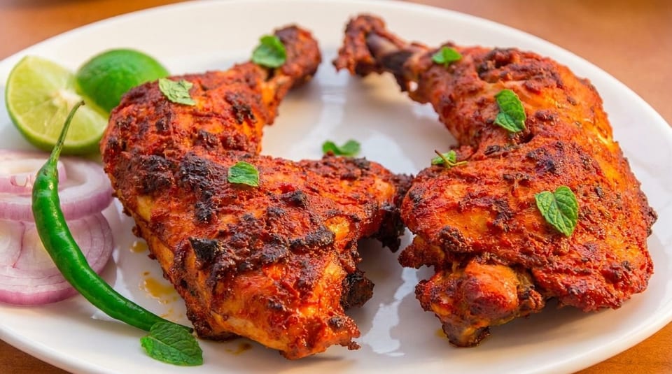 Two grilled chicken legs, garnished with mint, lime, red onion, and a green chili.